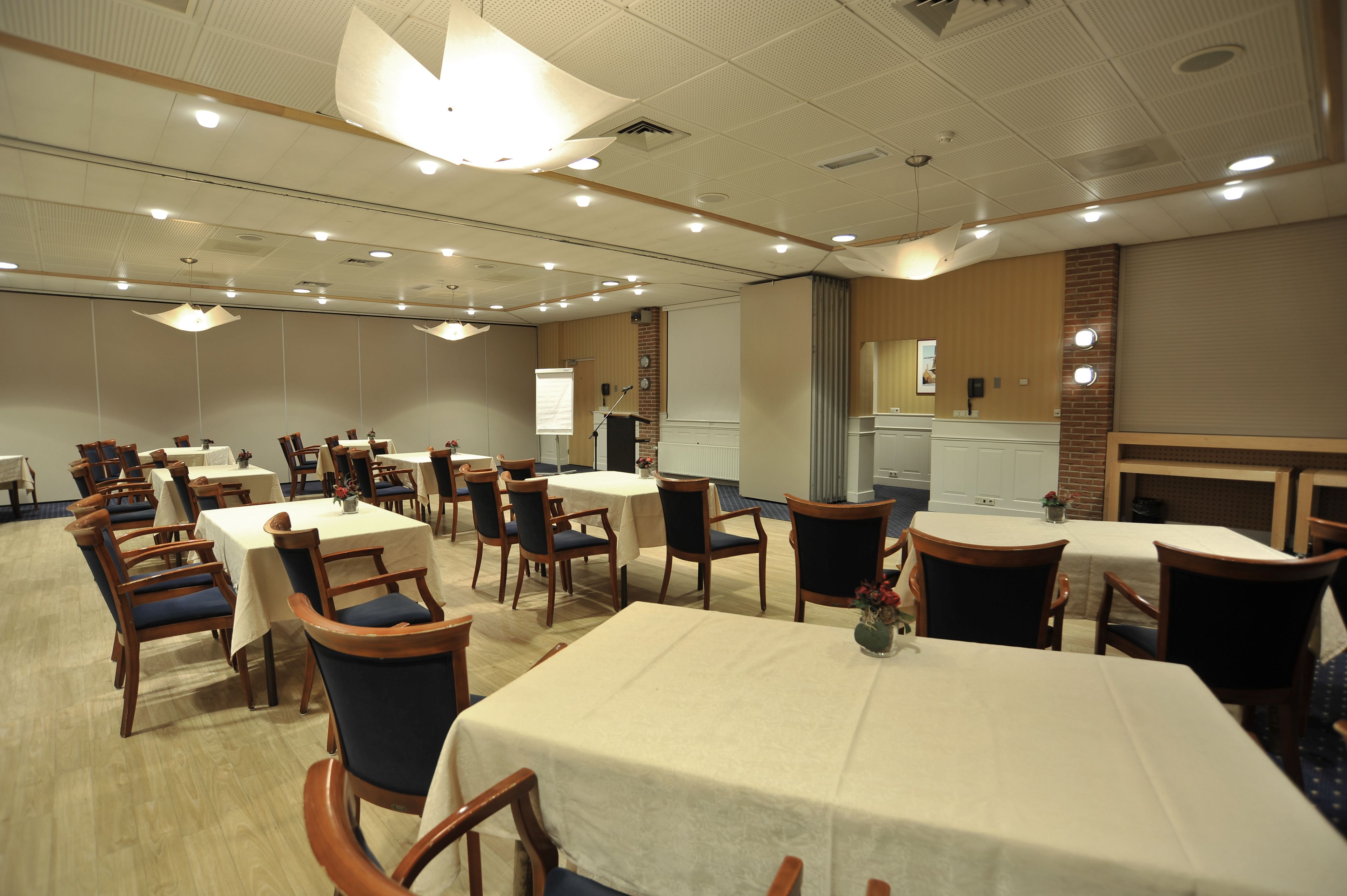A conference room with multiple tables and chairs, equipped with a projector and a presentation screen.
