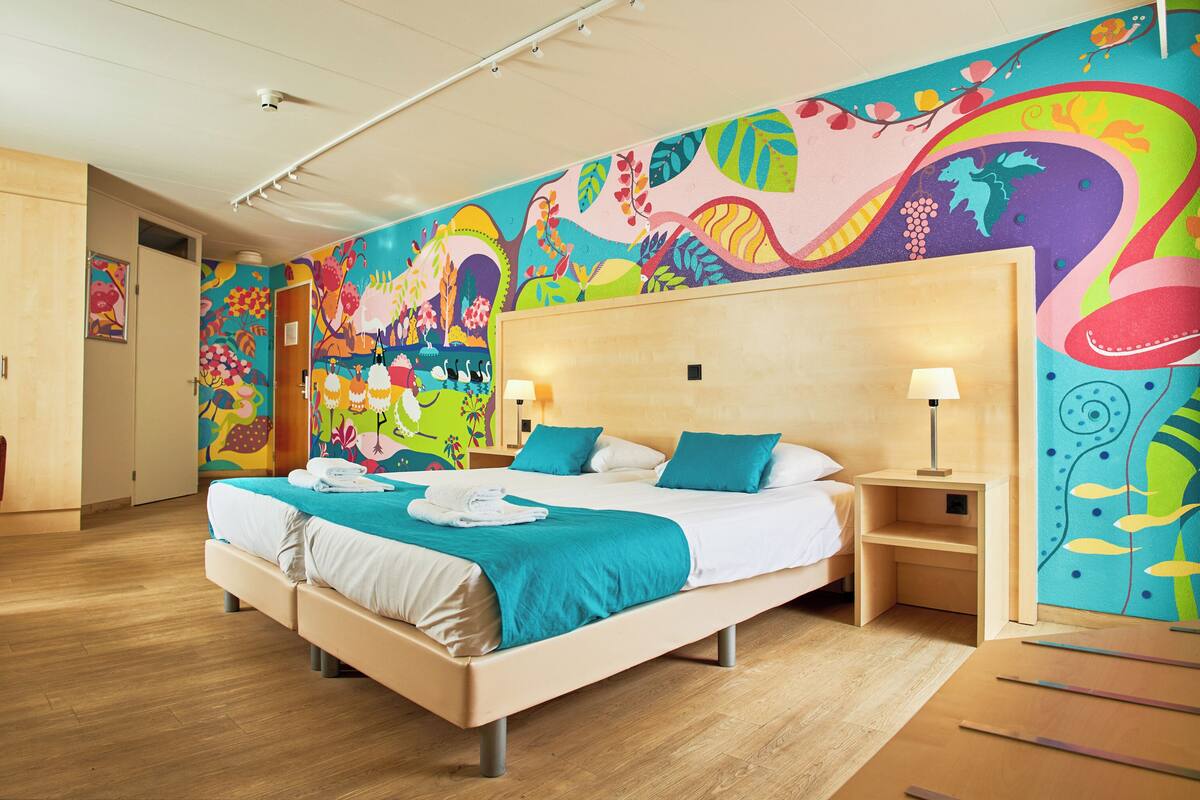 A hotel room with a large bed, two bedside tables, and a colorful mural on the wall.