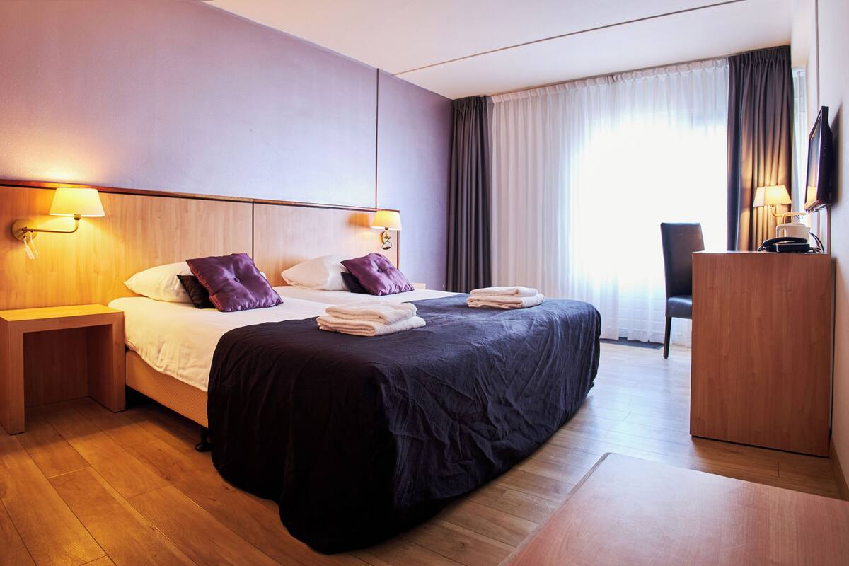 A hotel room with a large bed, two bedside lamps, a flat-screen TV, and a wooden desk.