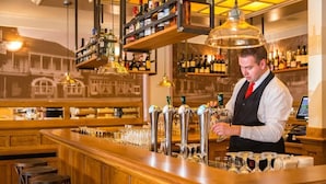 Zona de bar con múltiples grifos, taburetes y estanterías llenas de botellas.