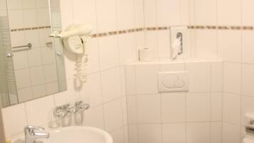 Un baño con lavamanos blanco, inodoro, espejo y secador de pelo montado en la pared.