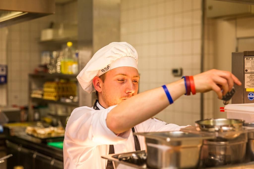 A chef in a professional kitchen with stainless steel appliances and a tiled backsplash.