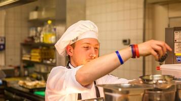 A chef in a professional kitchen with stainless steel appliances and a tiled backsplash.