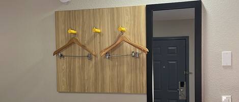 A room with a wooden wall-mounted coat rack, a mirror, a white bench with a blue drawer, and a door.