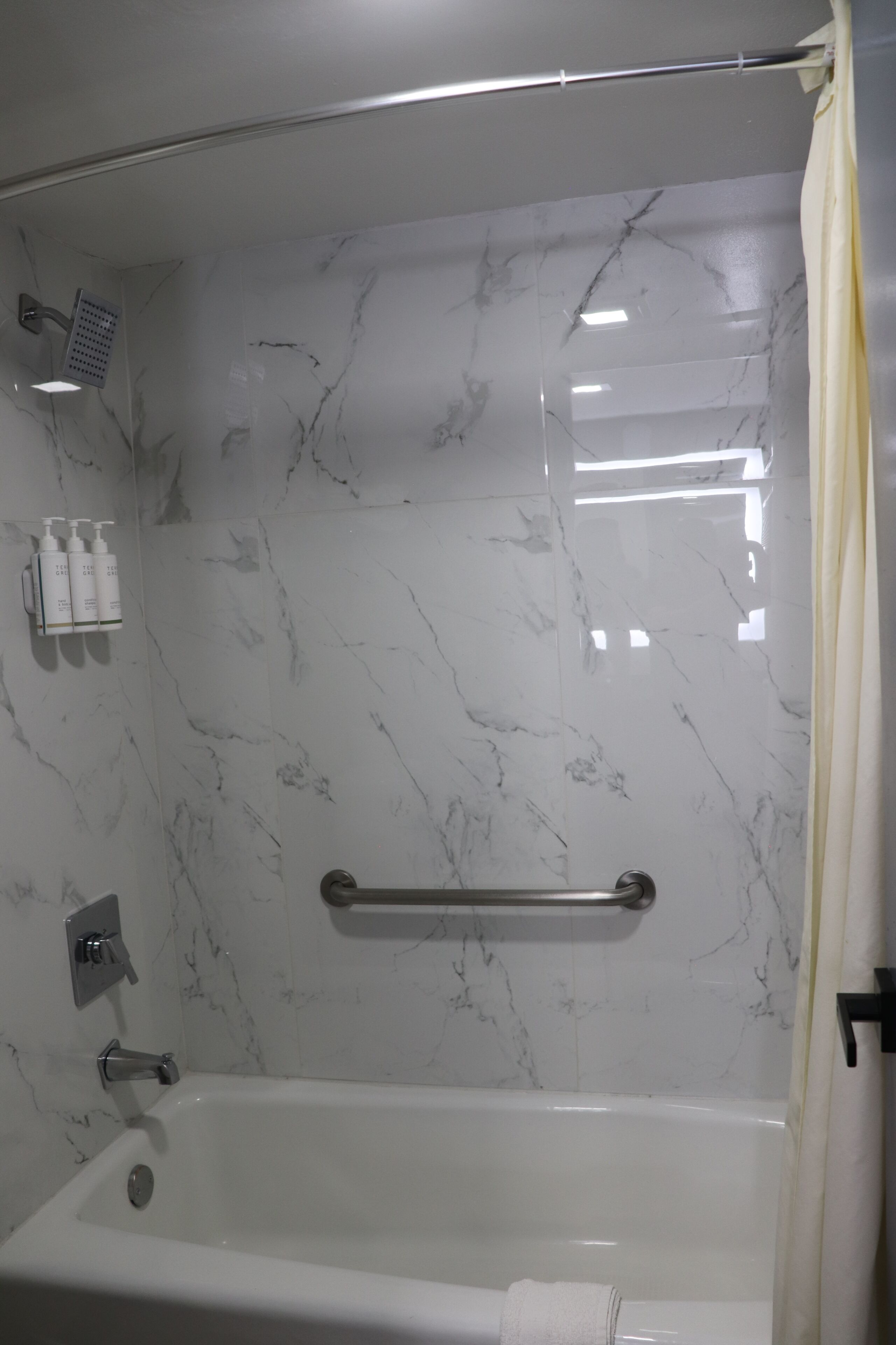 A bathroom with a bathtub, a shower, and a handrail.