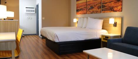 A hotel room with a bed, bedside tables, a desk with a chair, a sofa, and a wall-mounted air conditioner.