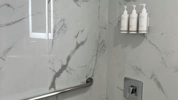 Een badkamer met een marmeren wand, een badkuip, een handgreep, een douchekop en drie flessen Terra Green producten.