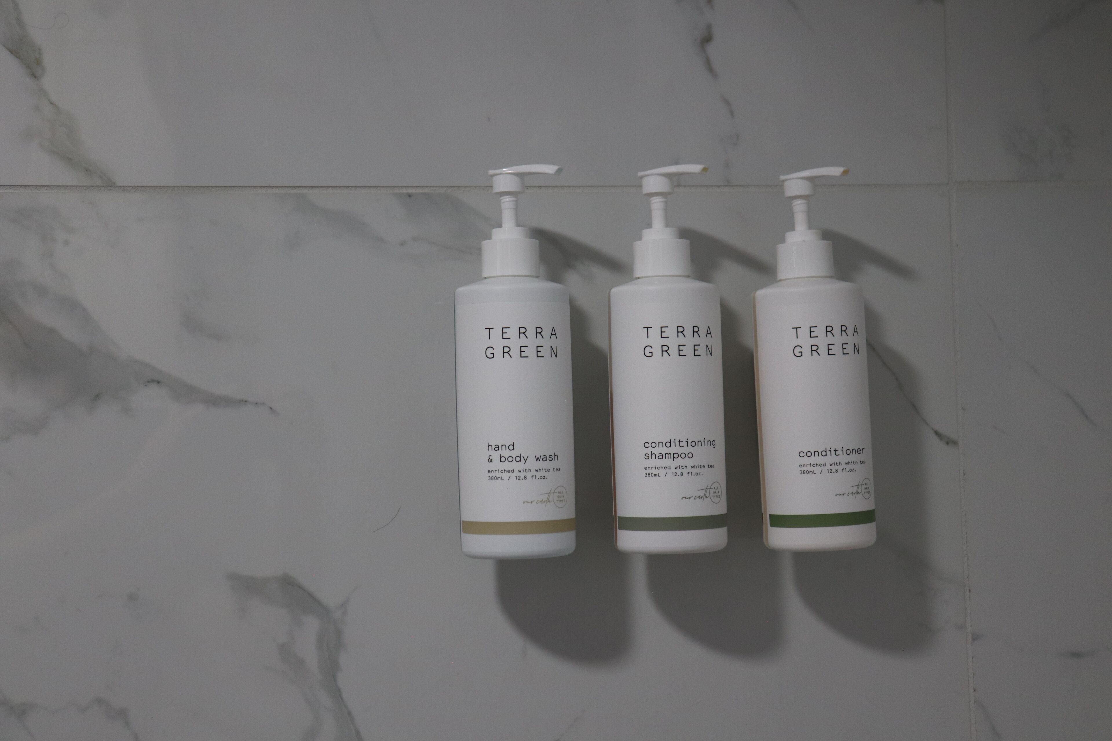 Tre flaconi di detergente e balsamo corpo e mani Terra Green su una superficie in marmo.