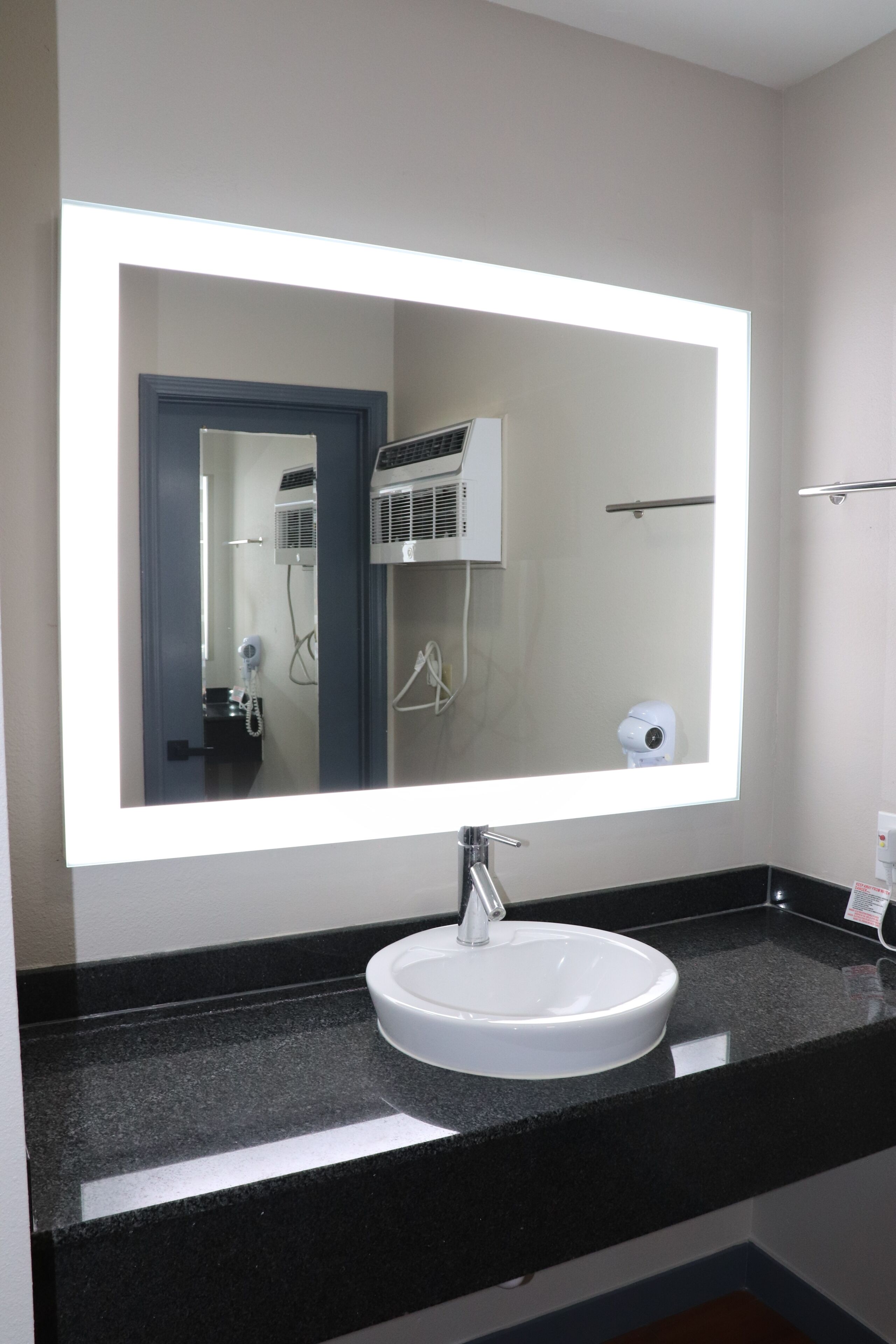 Un baño con un espejo grande, un lavabo blanco y un secador de pelo.