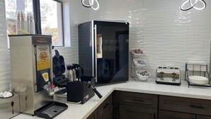 Una cucina con un distributore per pastella di waffle, una macchina per il caffè, un tostapane e un frigorifero.