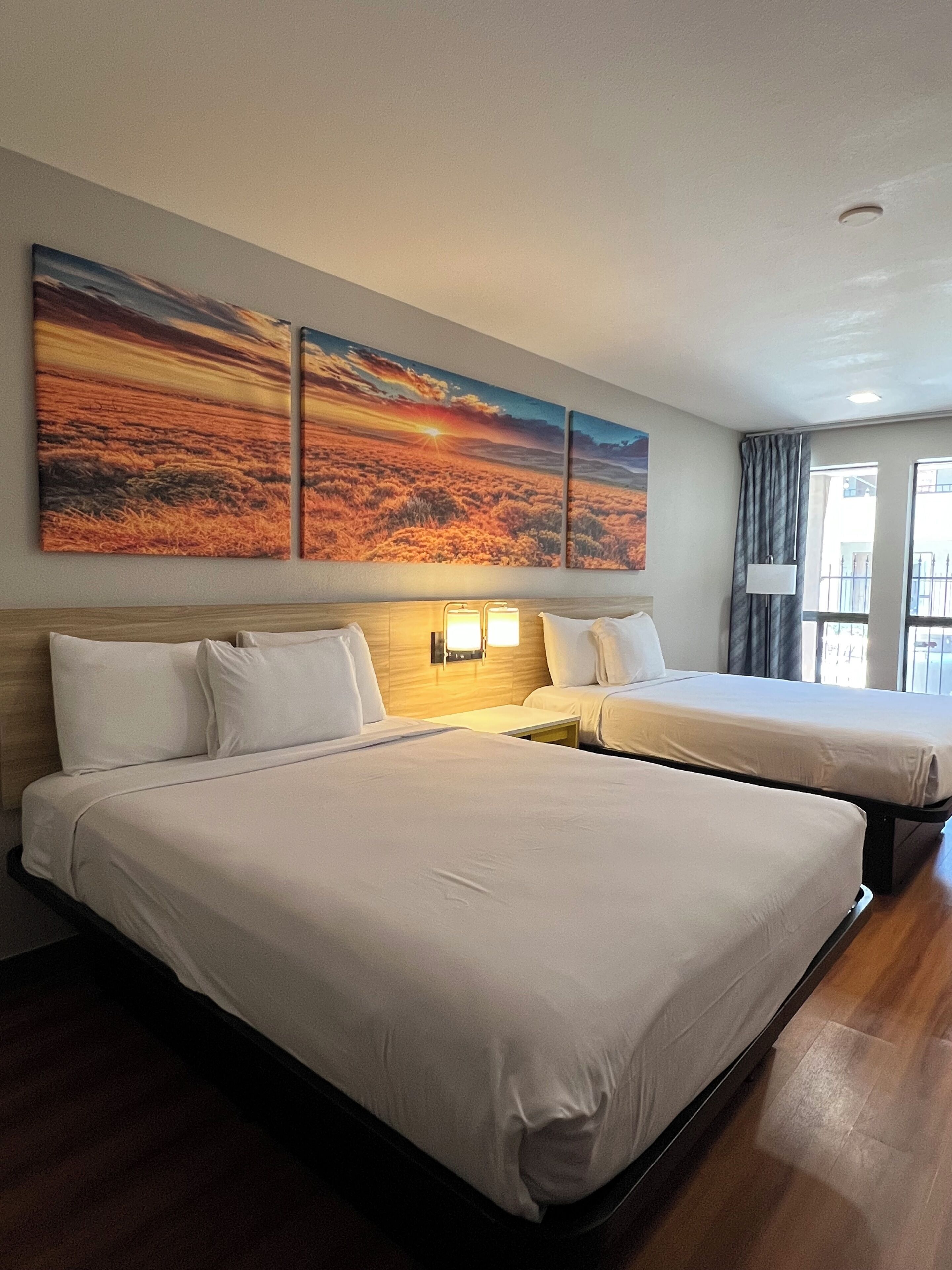 A hotel room with two beds, a wooden headboard, and a large window.