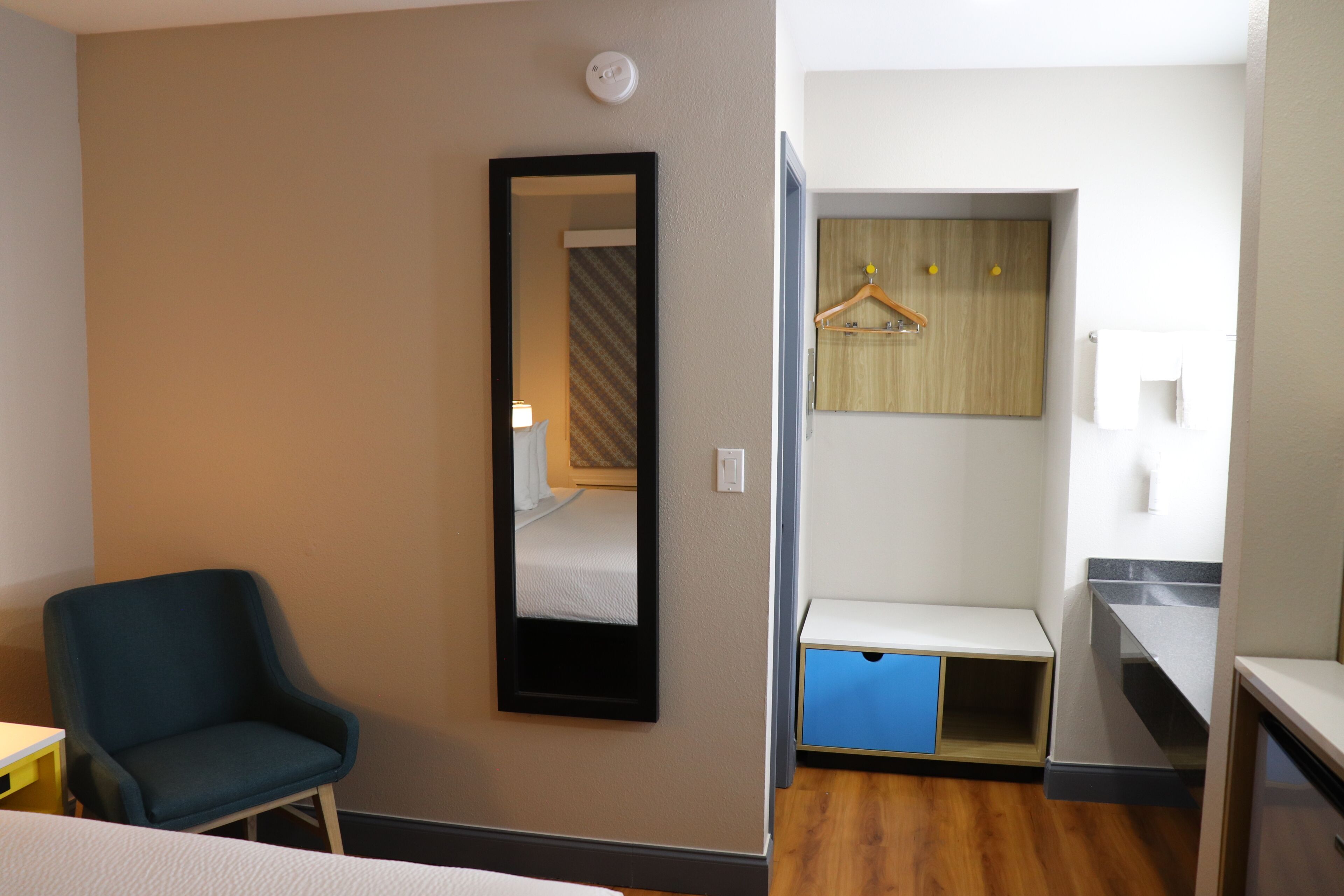 Een hotelkamer met een bed, een stoel, een spiegel, een kledingkast en een klein bureau.