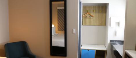 Een hotelkamer met een bed, een stoel, een spiegel, een kledingkast en een klein bureau.