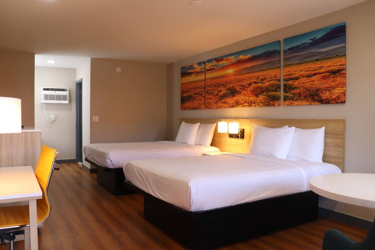 A hotel room with two beds, a desk, a chair, and a wall-mounted TV.