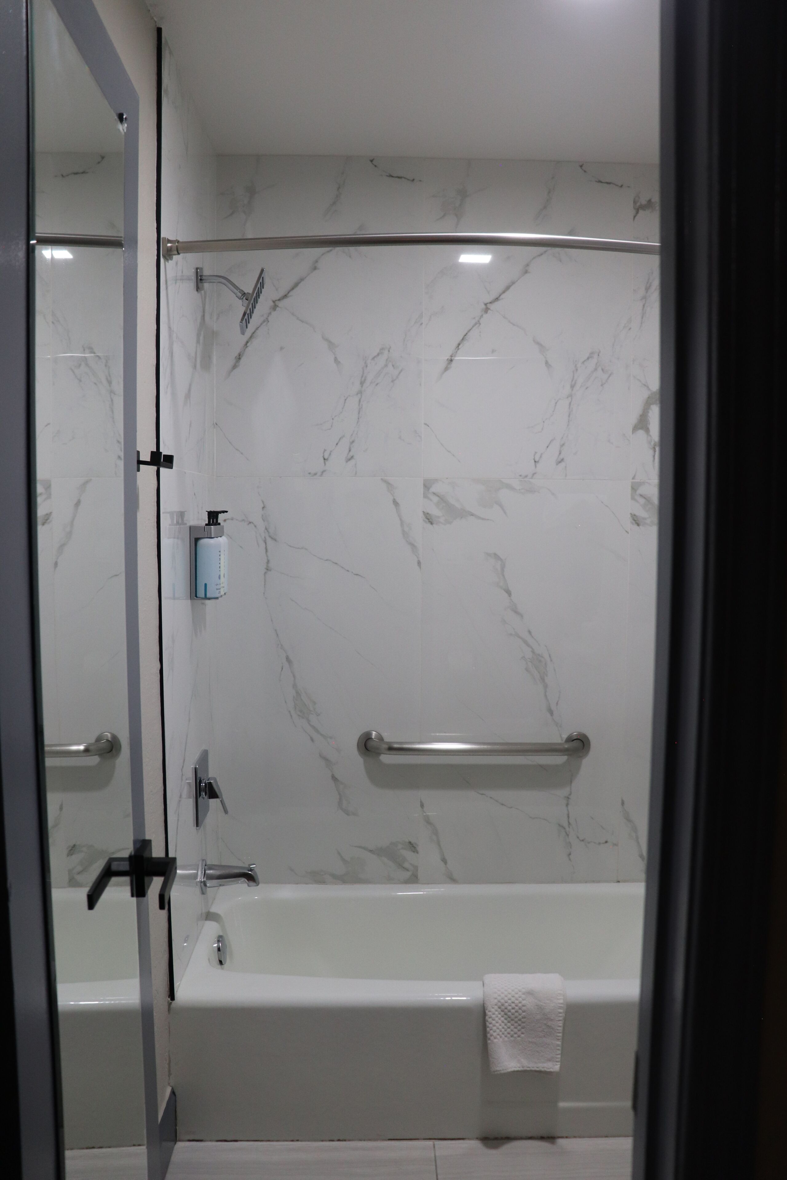 A bathroom with a bathtub, a glass shower enclosure, marble walls, and a towel rack.
