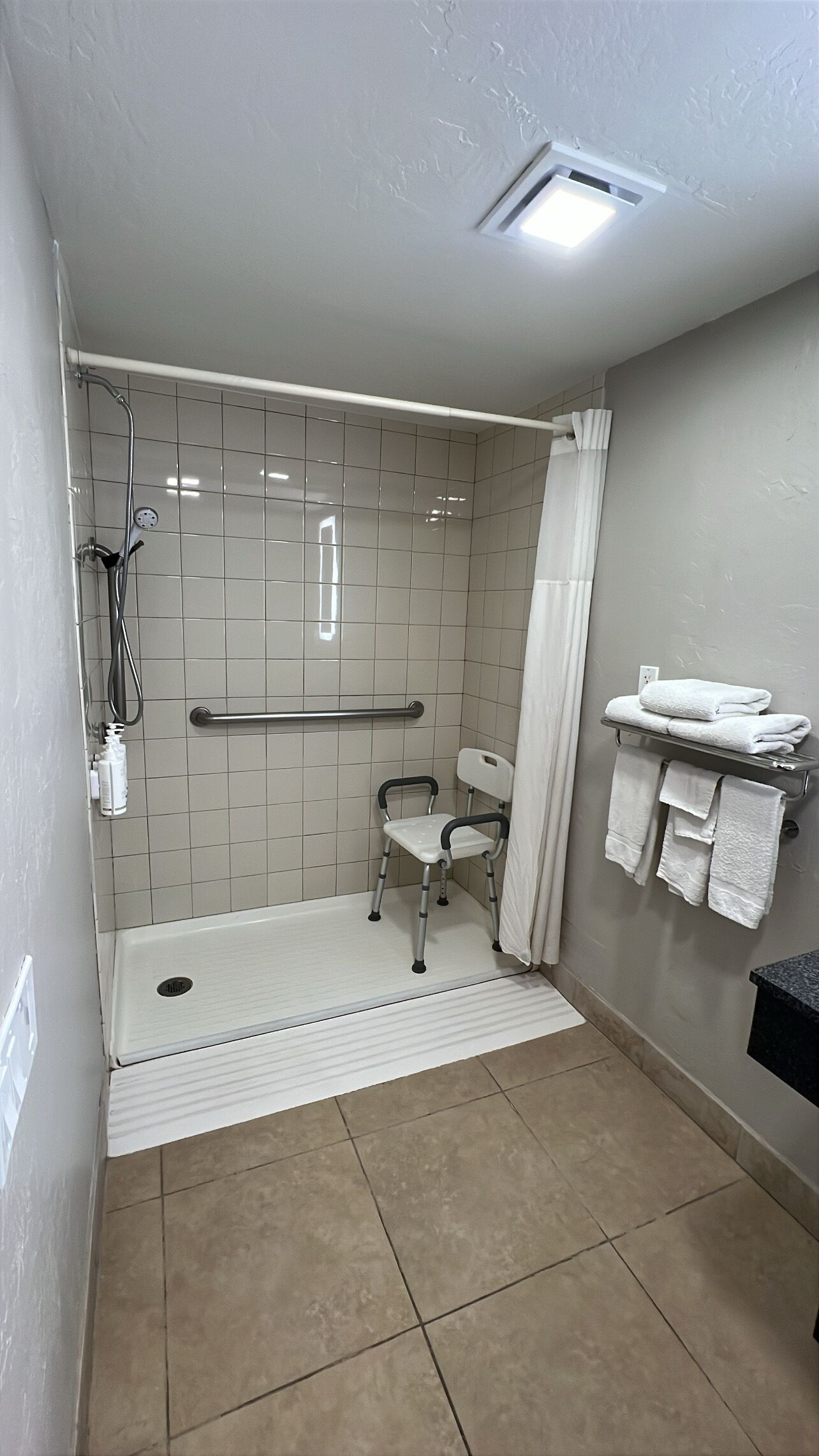 A bathroom with a walk-in shower, grab bar, and a wheelchair-accessible chair.