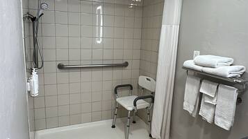 A bathroom with a walk-in shower, grab bar, and a wheelchair-accessible chair.