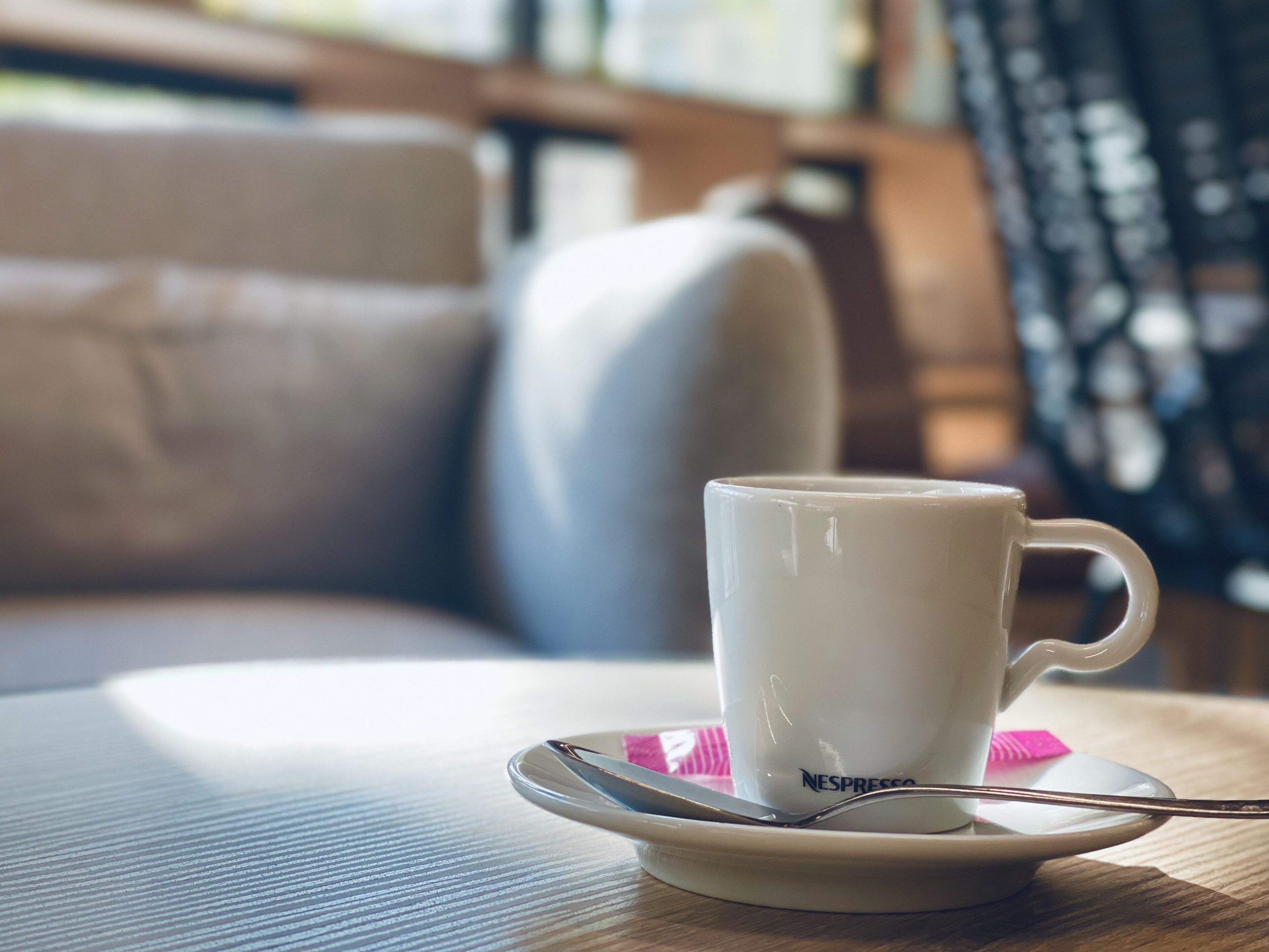 Une tasse blanche avec une cuillère posée sur une soucoupe, portant l’inscription « NESPRESSO », sur une table.