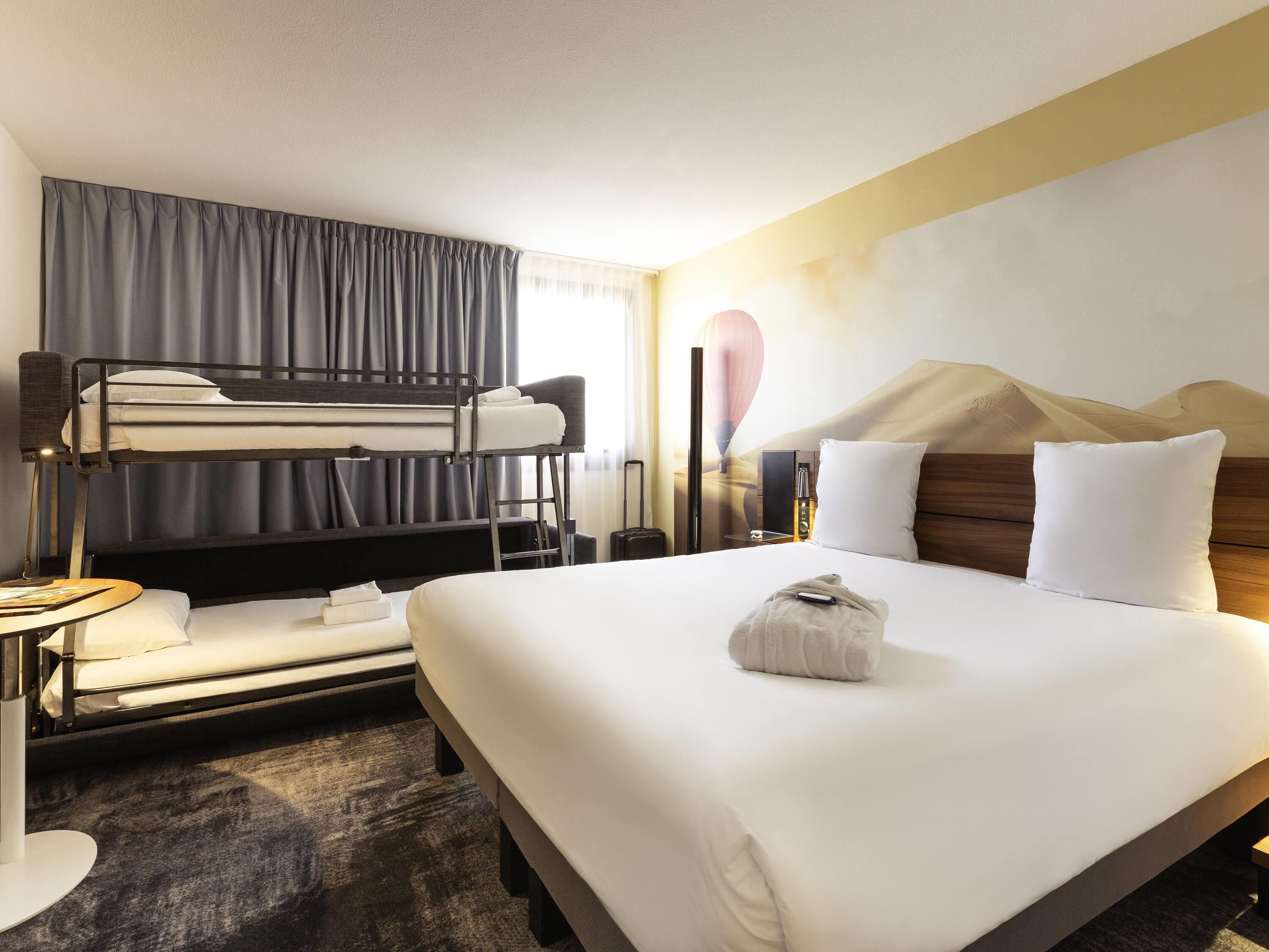 A hotel room with a bunk bed, a large bed, a desk, and a lamp.