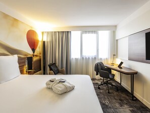 A hotel room with a bed, a desk, a chair, a TV, and a hot air balloon decoration. - Novotel Bordeaux Centre Gare Saint Jean (Bordeaux)