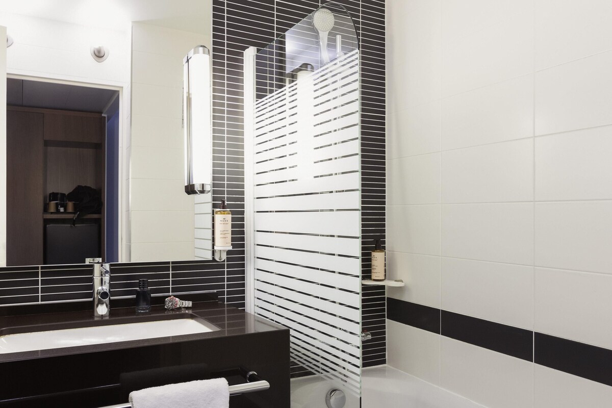 A modern bathroom with a black and white tiled wall, a large mirror, a black sink, and a glass shower enclosure.