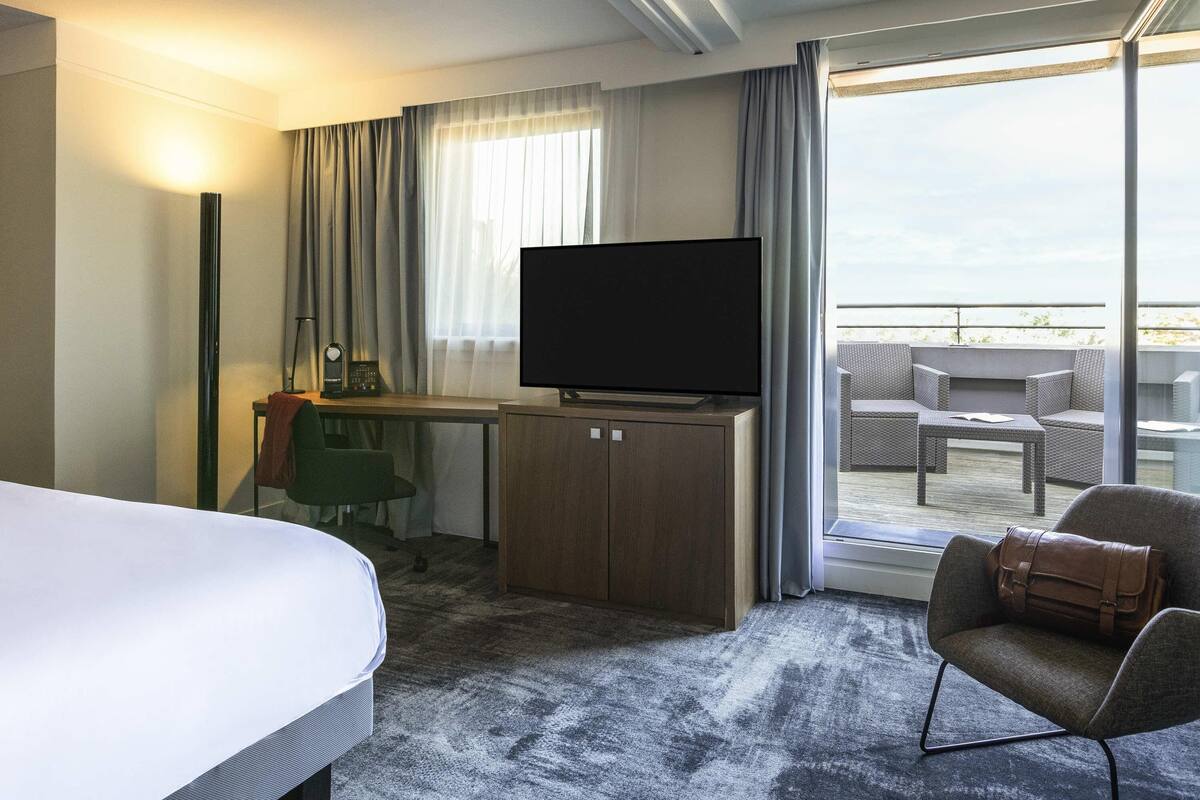 Ein Hotelzimmer mit Bett, Schreibtisch mit Fernseher, Stuhl und Balkon mit Sitzgelegenheit.