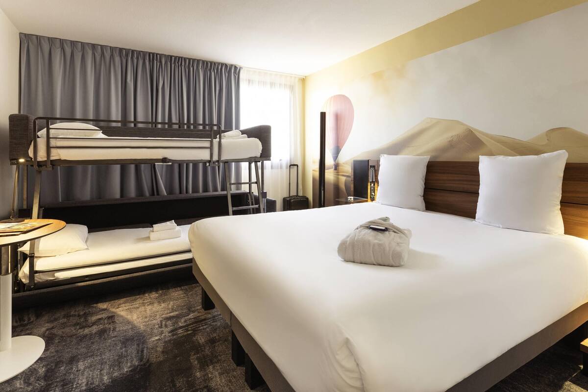 Ein Hotelzimmer mit Etagenbett, einem großen Bett, einem Schreibtisch mit Lampe und einem Wandheizgerät.