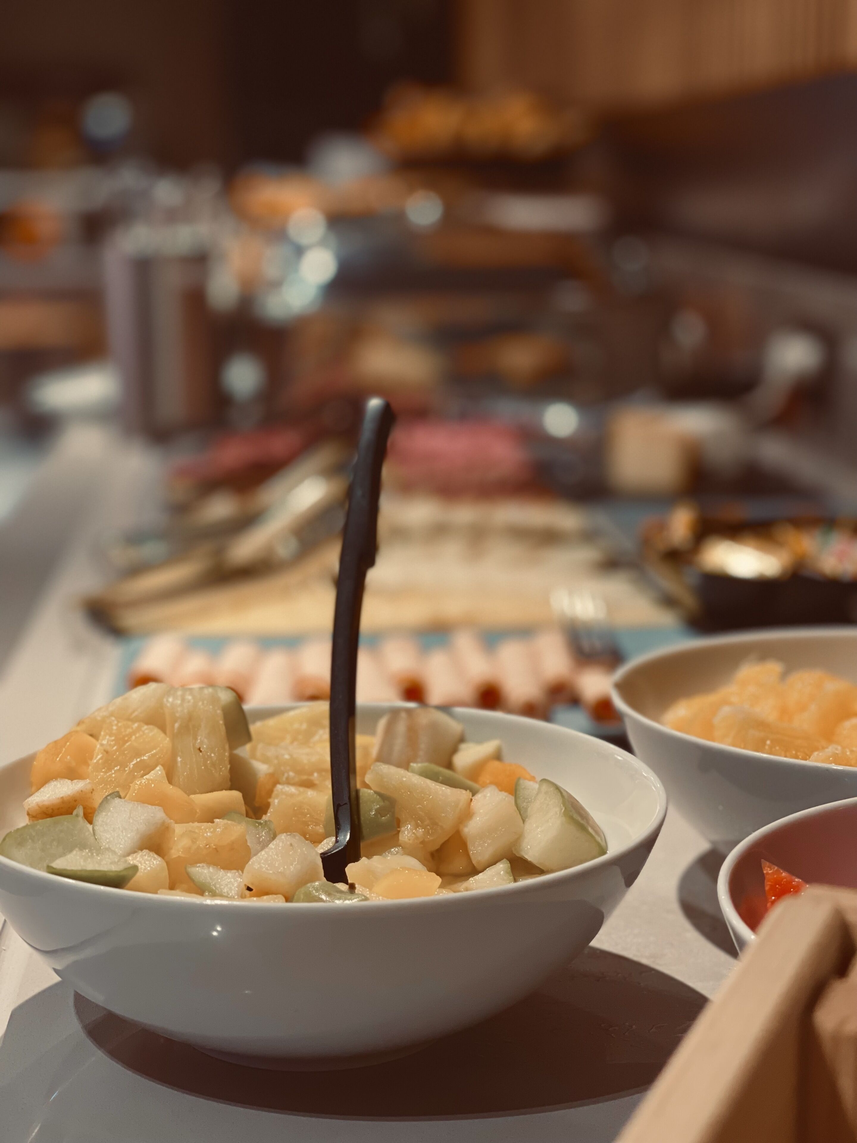 Ein reichhaltiges Buffet mit verschiedenen Speisen, darunter eine Schüssel Obstsalat mit einem Löffel.