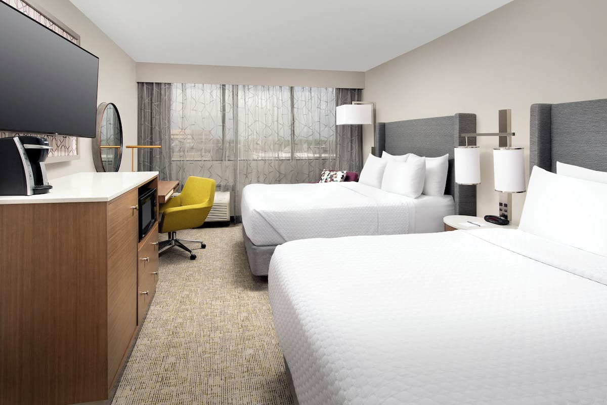 Une chambre d’hôtel avec deux lits, un bureau, une chaise, une télévision et une fenêtre avec des rideaux.