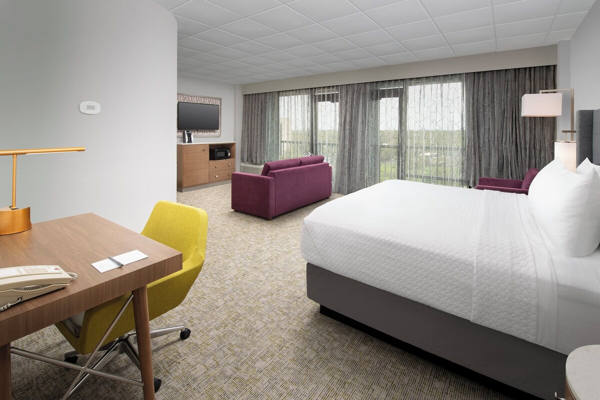A hotel room with a bed, a desk with a telephone, a chair, a television, and a window with curtains.