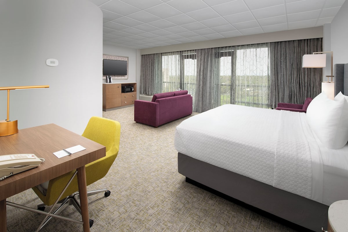 Une chambre d’hôtel avec un grand lit, un bureau avec un téléphone, une chaise, un téléviseur et une vue sur l’extérieur par les fenêtres.