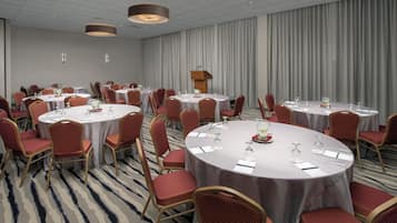 A conference room with round tables, red upholstered chairs, and a podium.