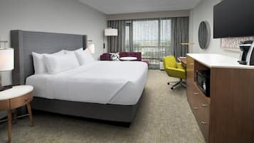 A hotel room with a large bed, a desk, a chair, a television, and a window with curtains.