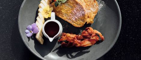 Un plato con un huevo frito, tocino, fresas y una taza pequeña de salsa.