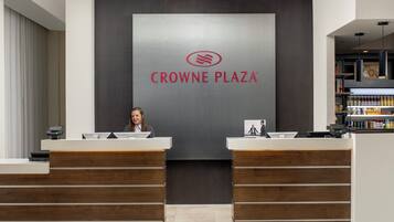Un comptoir d’accueil avec une enseigne indiquant « CROWNE PLAZA » et une femme assise derrière.