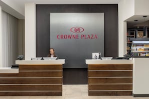 Vastaanottotiski, jossa on kyltti, jossa lukee ”CROWNE PLAZA”, ja sen takana istuu nainen.