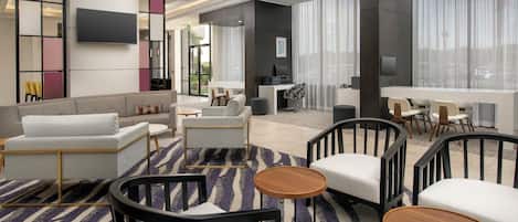A modern hotel lobby with a sofa, chairs, a dining area, and a large window.