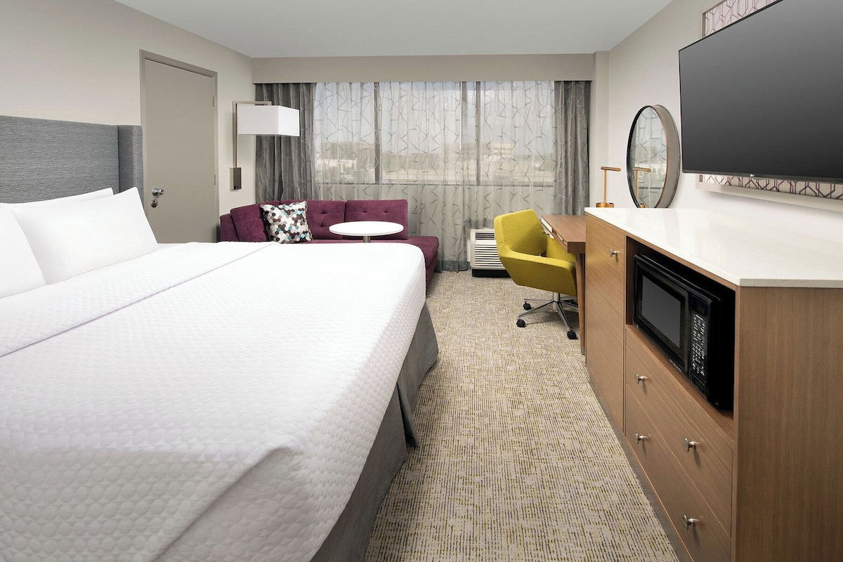 A hotel room with a large bed, a desk with a flat-screen TV, a chair, and a microwave.