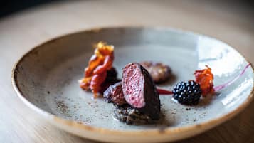 A plate with a slice of meat, some berries, and a small piece of red garnish.