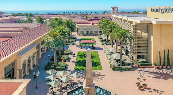 A hotel courtyard with a central fountain, palm trees, outdoor seating, and a view of the ocean.