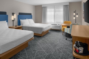 A hotel room with two beds, a desk, a chair, a coffee machine, and a window with curtains.