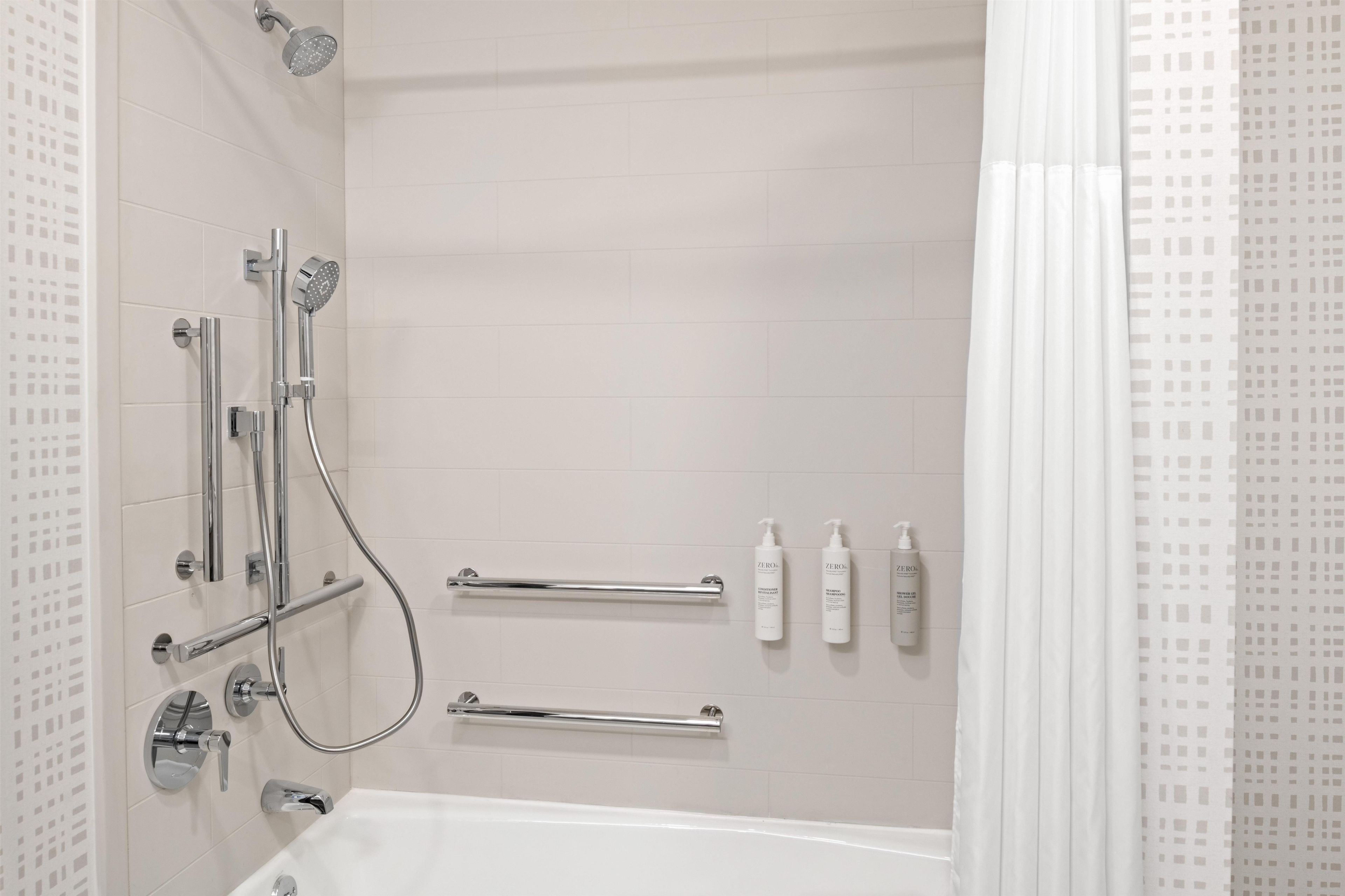 A modern bathroom with a bathtub, shower, and handrails.
