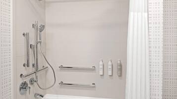 A modern bathroom with a bathtub, shower, and handrails.