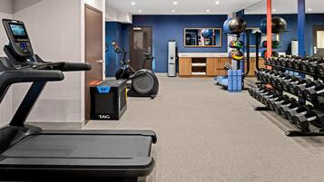 Gimnasio con equipo de ejercicio, incluyendo cinta de correr, bicicleta estática y varios pesas.