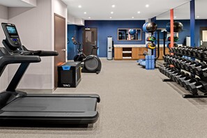 Een sportschool met trainingsapparatuur, waaronder een loopband, een hometrainer en diverse gewichten.
