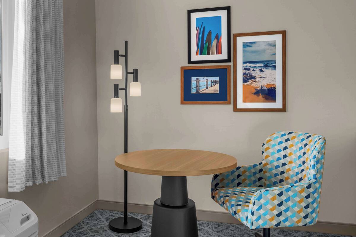 Una habitación con una mesa redonda de madera, un sillón estampado y tres cuadros en la pared.