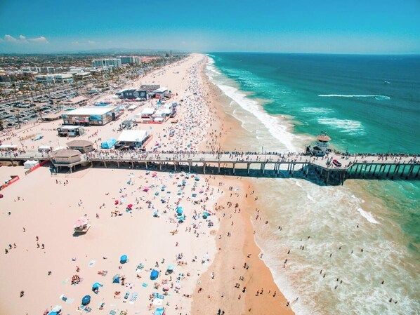 An aerial view of a beach with a pier, numerous umbrellas, and people. - Hampton Inn by Hilton Costa Mesa Newport Beach (Costa Mesa)
