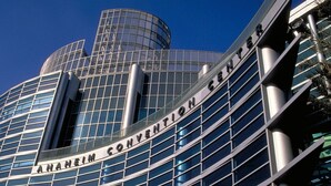 El exterior del Centro de Convenciones de Anaheim, con fachada de vidrio moderna y una estructura cilíndrica destacada.