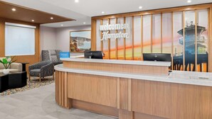 Mostrador de recepción de hotel con un cartel que dice 'Welcome to Hampton', zona de estar con una silla y vista a una escena costera.