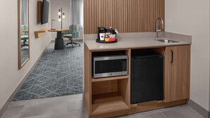 Habitación de hotel compacta con kitchenette, televisor de pantalla plana, un mueble de madera, microondas y lavabo.